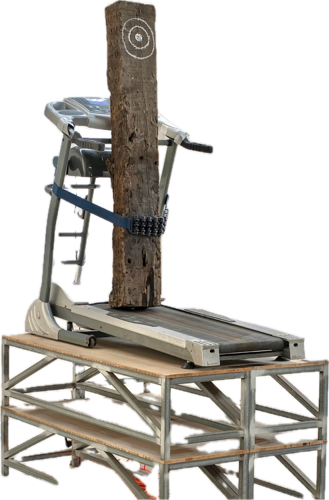 A weathered railway sleeper marked with a chalk target, strapped upright to a running treadmill on a steel table