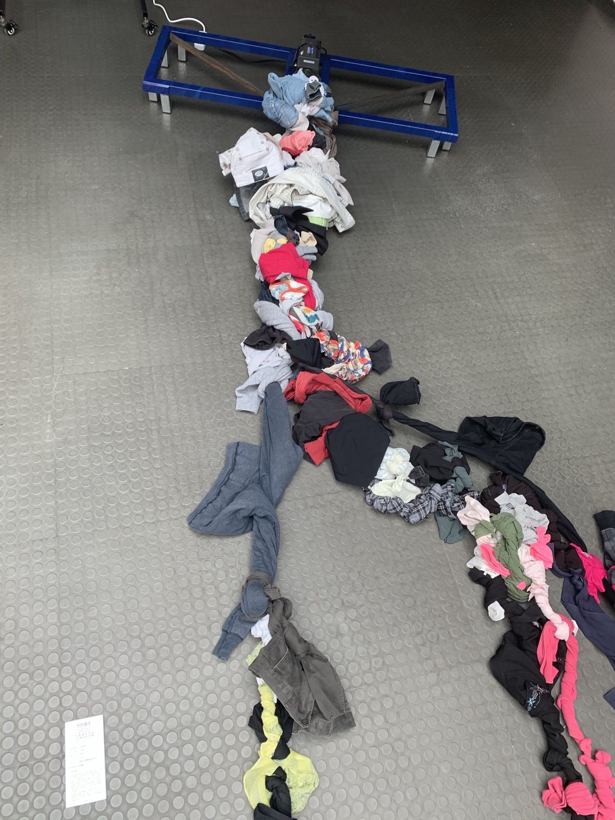 A chain of knotted clothes running across a grey floor to a blue steel frame with a motor