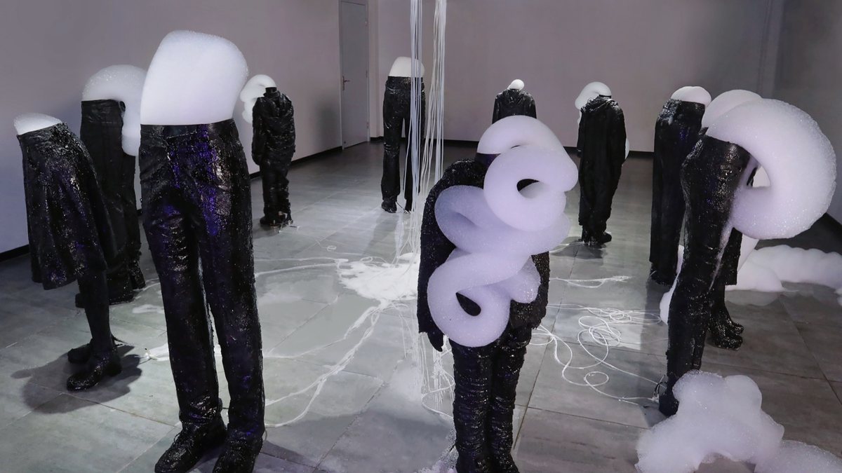 A room of black columns shaped like standing figures, some topped with white foam.
